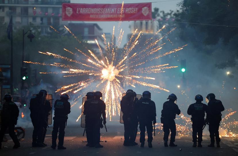 Des feux d'artifice éclatent devant les CRS lors des célébrations parisiennes.