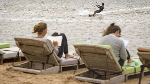 Deux vacanciers européens profitant d'un coucher de soleil sur une plage du Sahara occidental, tandis qu'un autre pratique le kitesurf dans l'océan